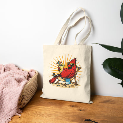 Tote bag with a cardinal design sitting on a wooden surface next to a pink blanket and plant.