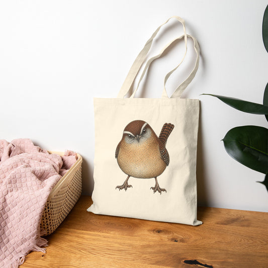 Tote bag with a carolina wren design on a wooden surface next to a pink blanket and plant.