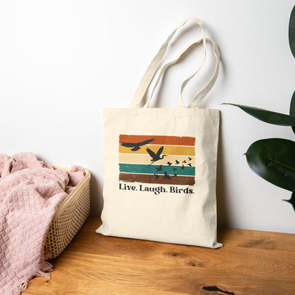 Tote bag with 'Live Laugh Birds' design on a wooden surface with a plant in the background