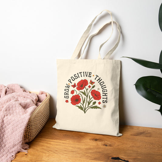 Tote bag with floral design and text, 'grow positive thoughts' on a wooden surface with a white wall background