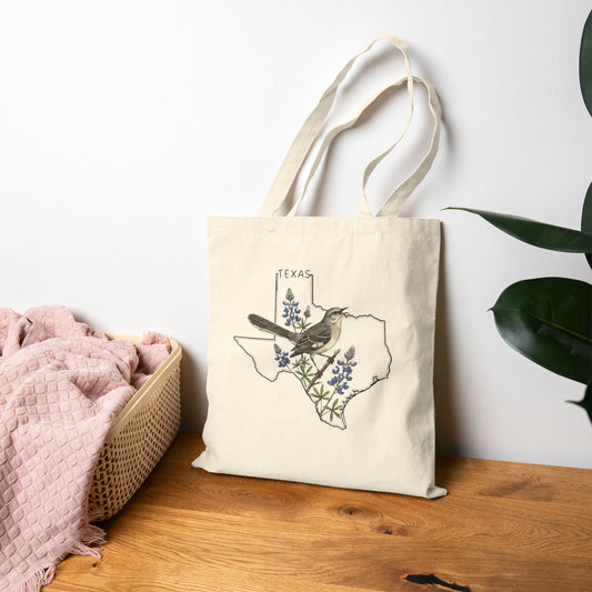 Tote bag with Texas design featuring a bird and flowers on a wooden surface.