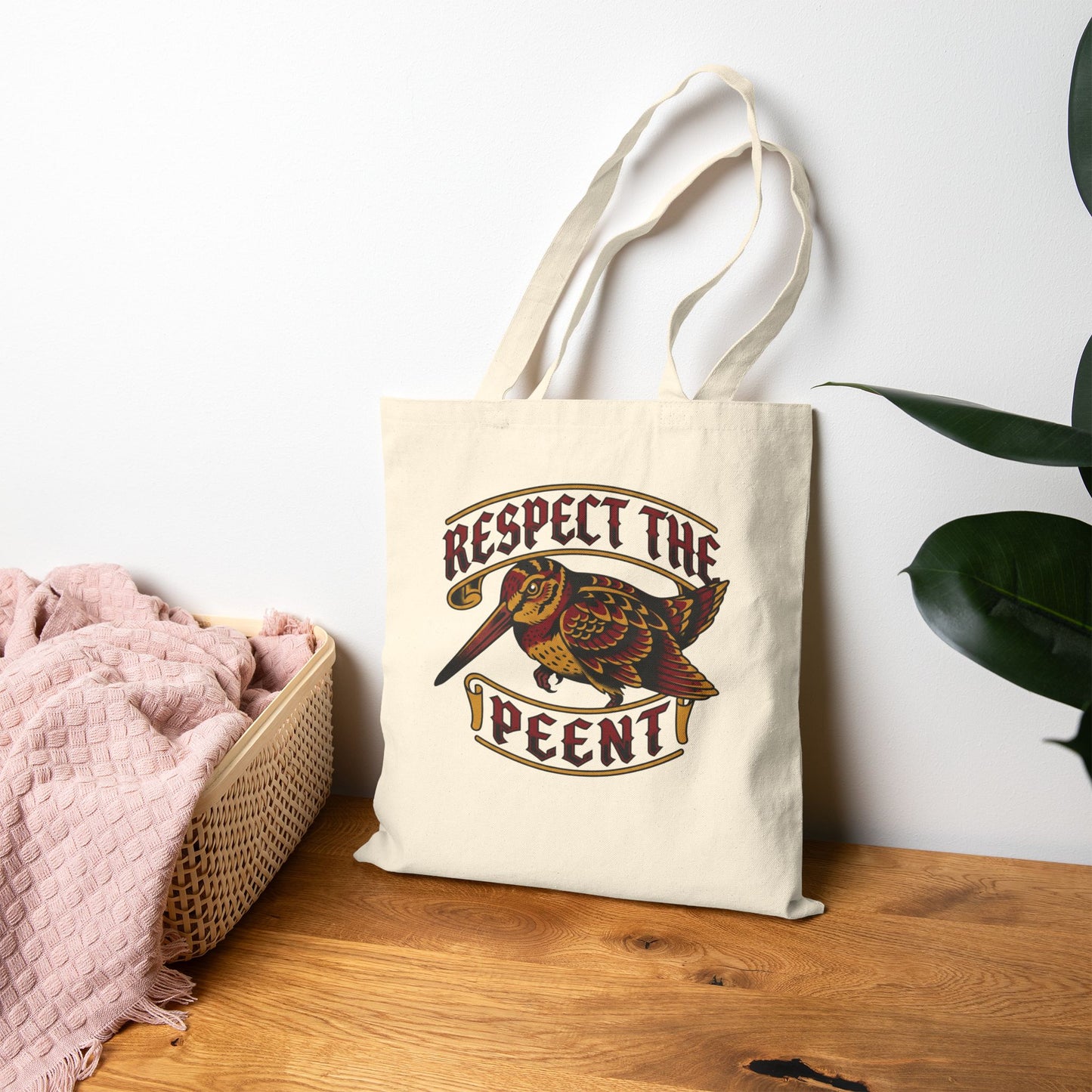 Tote bag with 'Respect the Peent' woodcock design on a wooden surface with a plant in the background