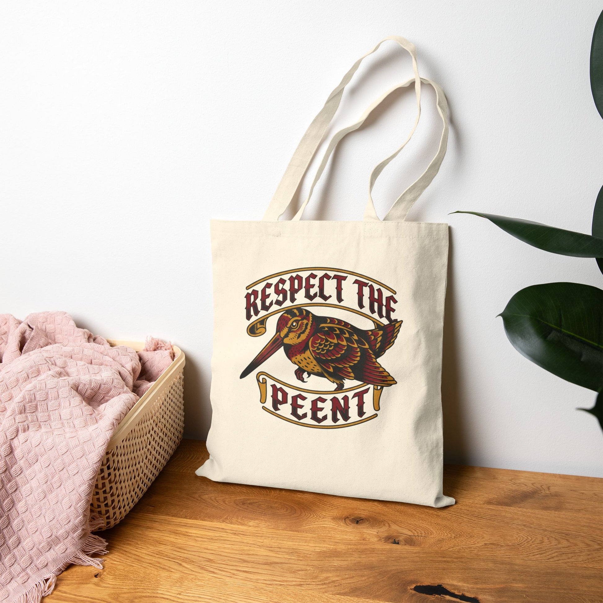 Tote bag with 'Respect the Peent' woodcock design on a wooden surface with a plant in the background