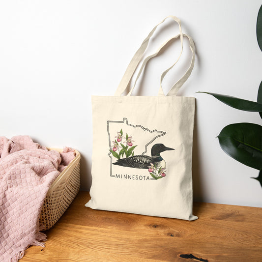 Tote bag with Minnesota loon design on a wooden surface with a plant in the background