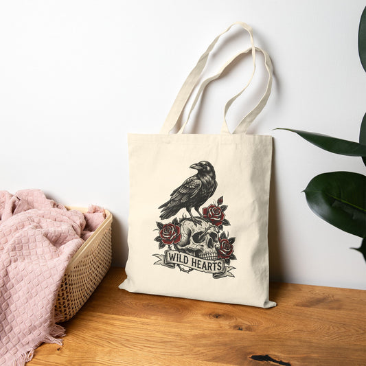 Tote bag with a design of a raven, skull, and roses on a wooden surface.
