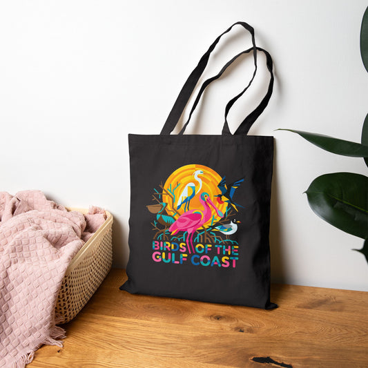 Black tote bag with colorful design and text 'Birds of the Gulf Coast' on a wooden surface.