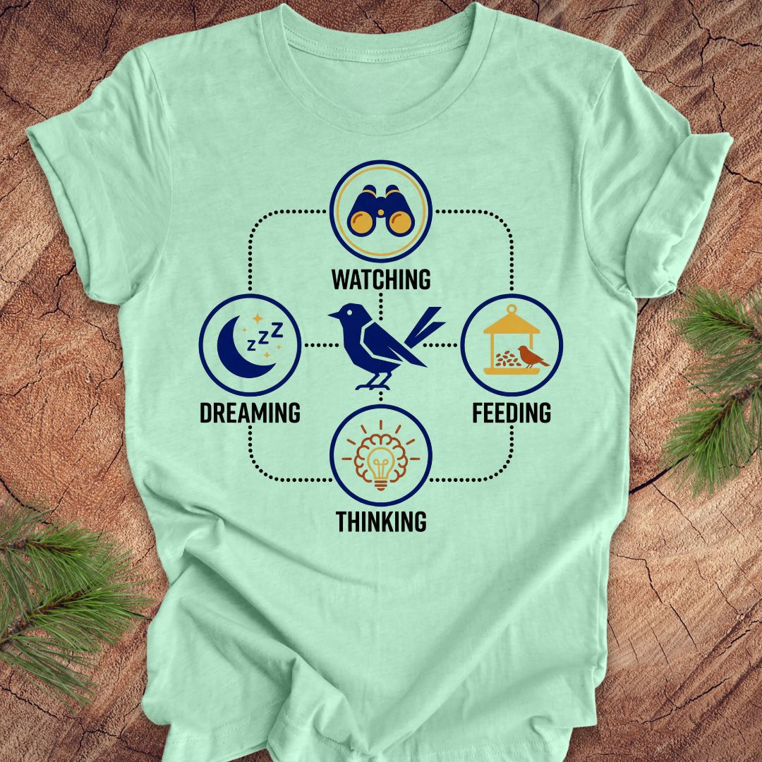 Mint green t-shirt with a bird graphic and "dreaming, watching, feeding, thinking" text and graphics on a wood background.