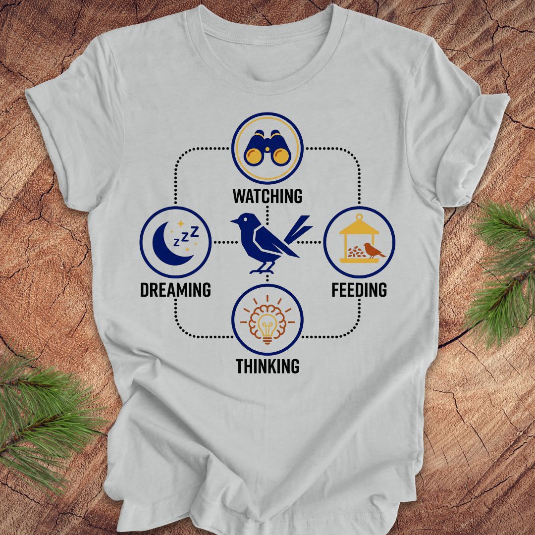 Gray t-shirt with a bird graphic and "dreaming, watching, feeding, thinking" text and graphics on a wood background.