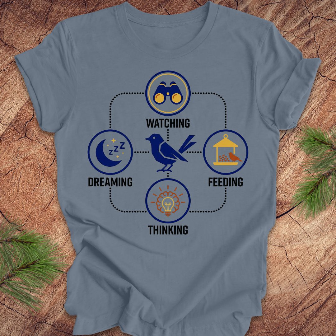 Steel blue t-shirt with a bird graphic and "dreaming, watching, feeding, thinking" text and graphics on a wood background.