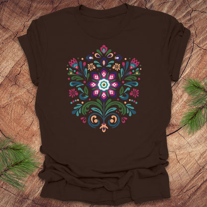 Brown t-shirt with a colorful dutch inspired floral design on a wood background.