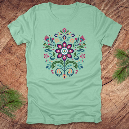Mint green t-shirt with a colorful dutch inspired floral design on a wood background.
