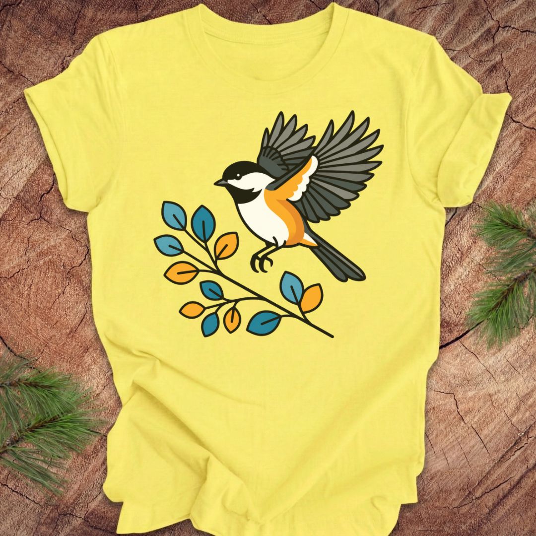 A bright yellow short-sleeve t-shirt laid flat on a rustic wood surface, featuring a graphic of a bird perched on a branch with blue, orange, and yellow leaves.