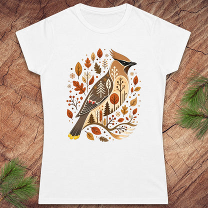 A white short-sleeve crewneck t-shirt featuring a detailed graphic of a cedar waxbird surrounded by autumn leaves and trees, displayed flat on a rustic wood background with pine branches in the corners.