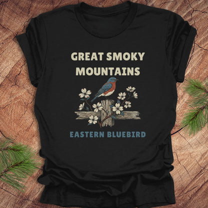 Black t-shirt with 'Great Smoky Mountains Eastern Bluebird' design on a wooden surface.