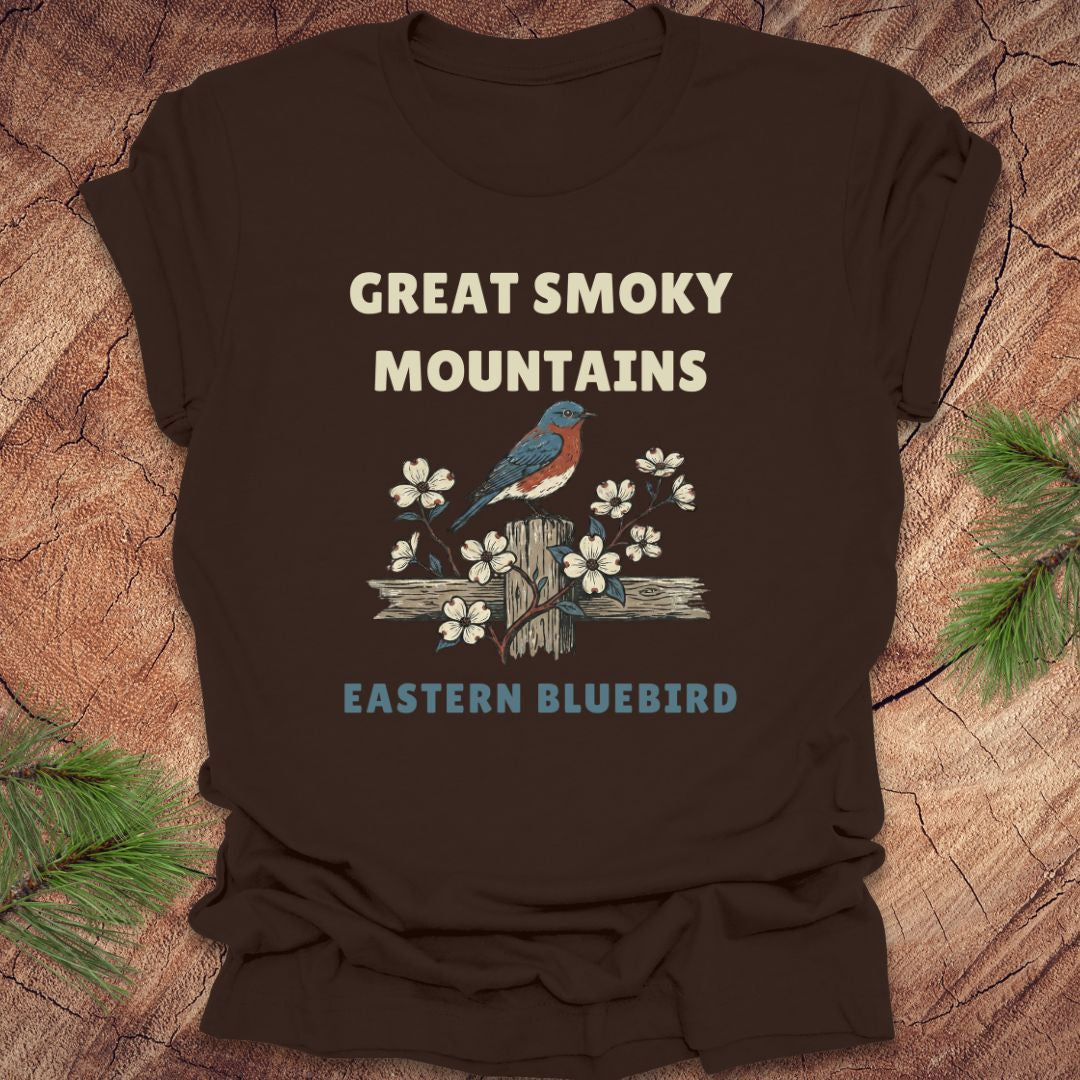 Brown t-shirt with 'Great Smoky Mountains' and 'Eastern Bluebird' design on a wooden surface.