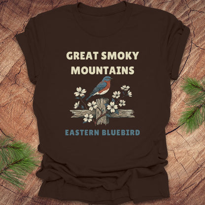 Brown t-shirt with 'Great Smoky Mountains' and 'Eastern Bluebird' design on a wooden surface.