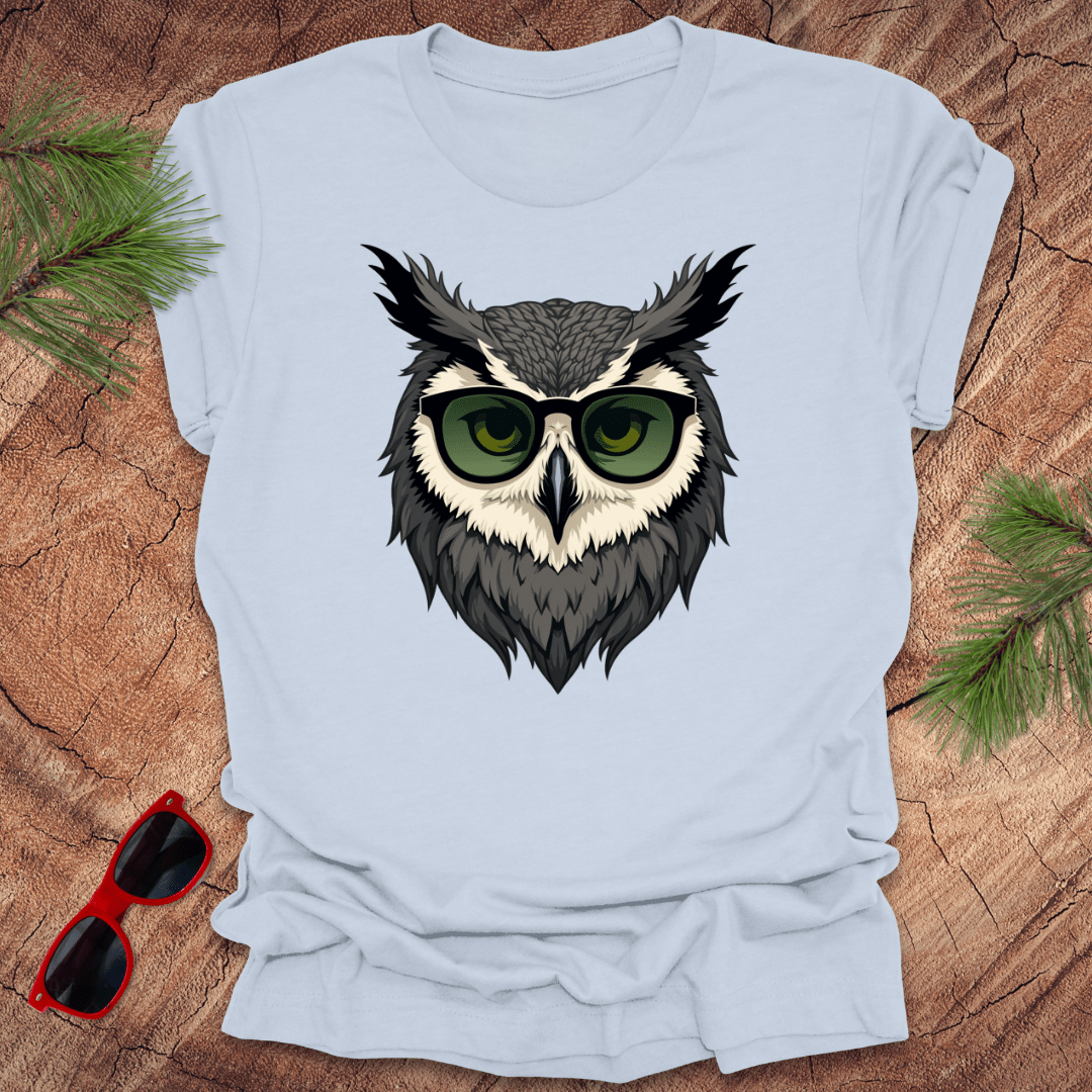 Light blue tshirt with a graphic of an owl head with sunglasses on. it is on a wood background.