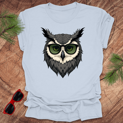 Light blue tshirt with a graphic of an owl head with sunglasses on. it is on a wood background.