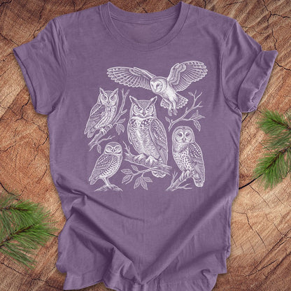 Purple t-shirt with white owl line-art illustrations on a wooden surface