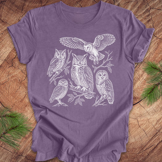 Purple t-shirt with white owl line-art illustrations on a wooden surface