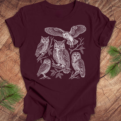 Maroon t-shirt with white owl line-art illustrations on a wooden surface