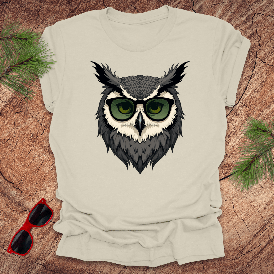 Beige tshirt with a graphic of an owl head with sunglasses on. it is on a wood background.