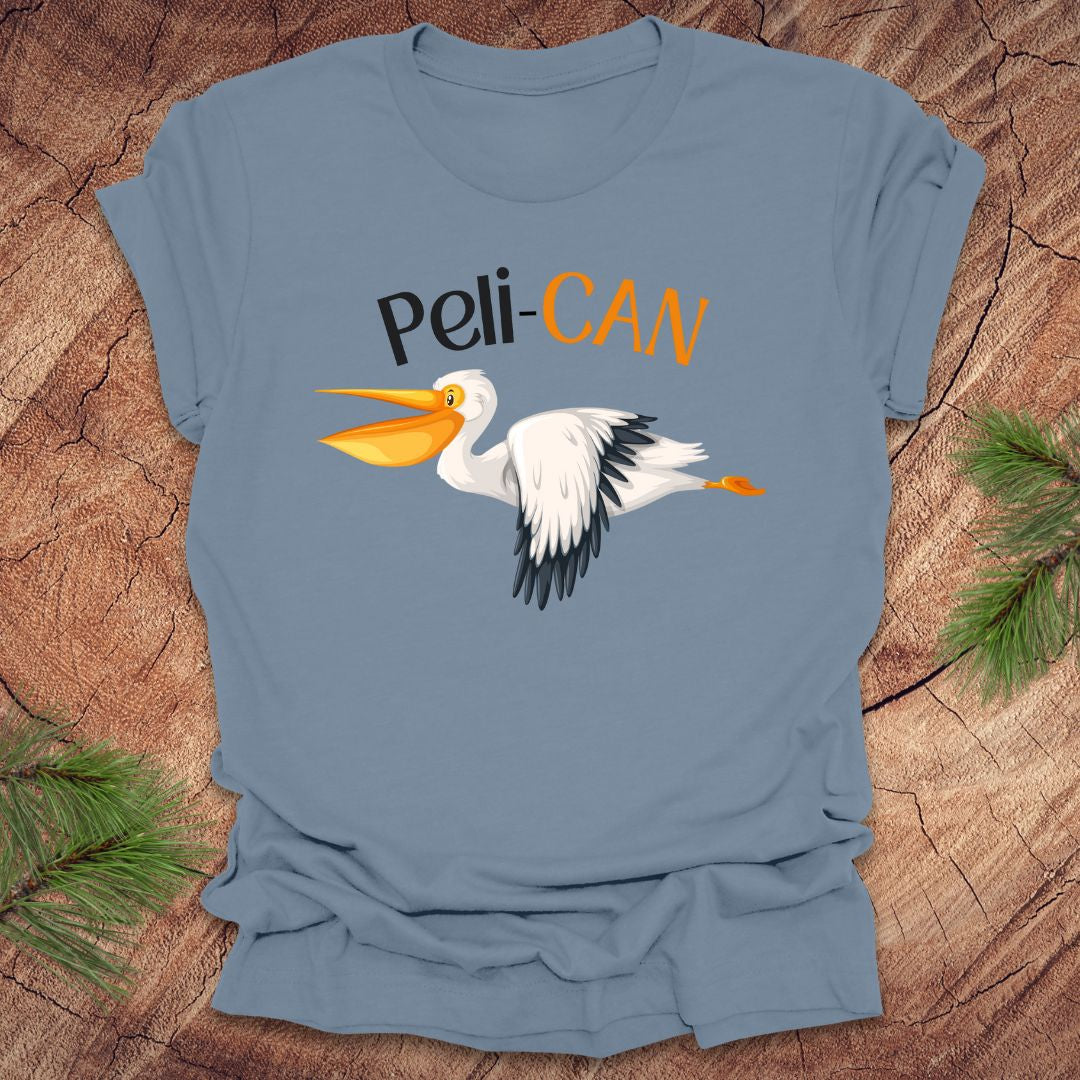 Blue t-shirt with a pelican graphic and 'Peli-CAN' text on a wooden surface.