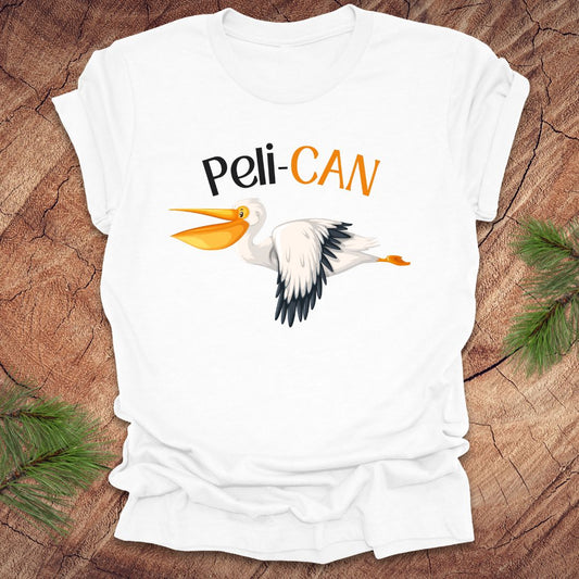 White t-shirt with a pelican graphic and 'Peli-CAN' text on a wooden surface.