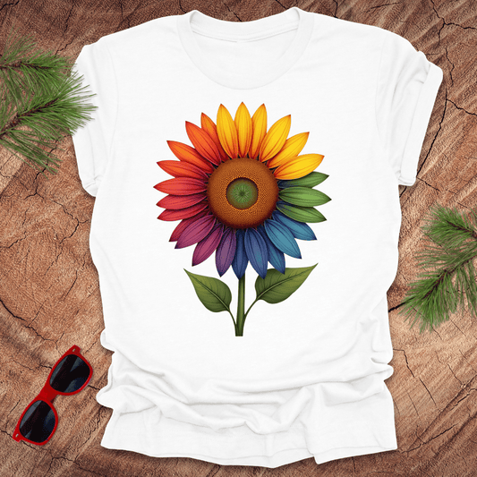 White tshirt with a bold rainbow sunflower graphic on a wood background.