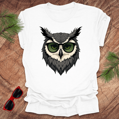 White tshirt with a graphic of an owl head with sunglasses on. it is on a wood background.
