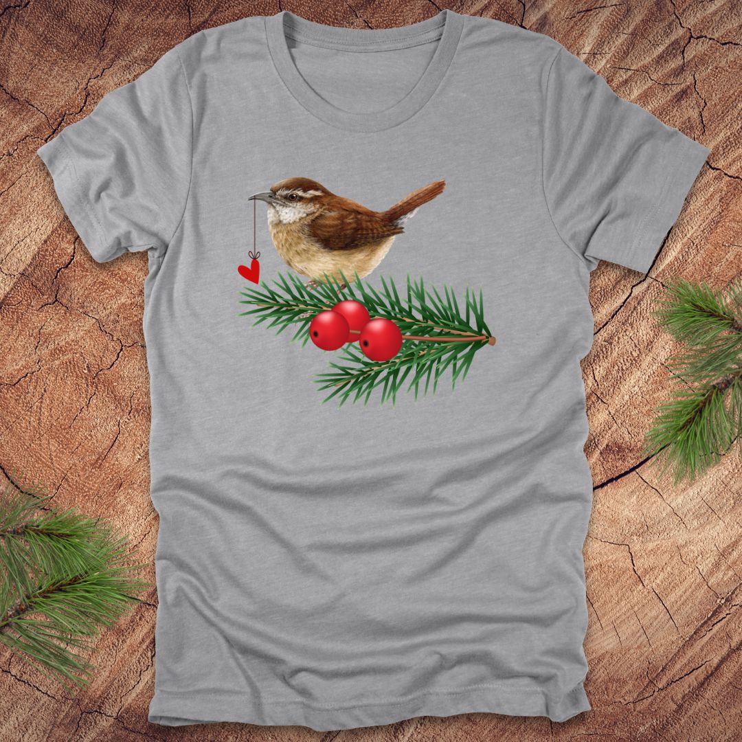 Gray t-shirt with a wren bird holding a heart on a string and holly design on a wooden surface