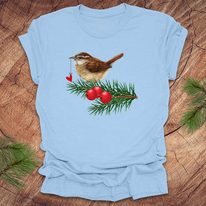 Baby blue t-shirt with a wren bird holding a heart on a string and holly design on a wooden surface