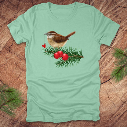 Mint green t-shirt with a wren bird holding a heart on a string and holly design on a wooden surface