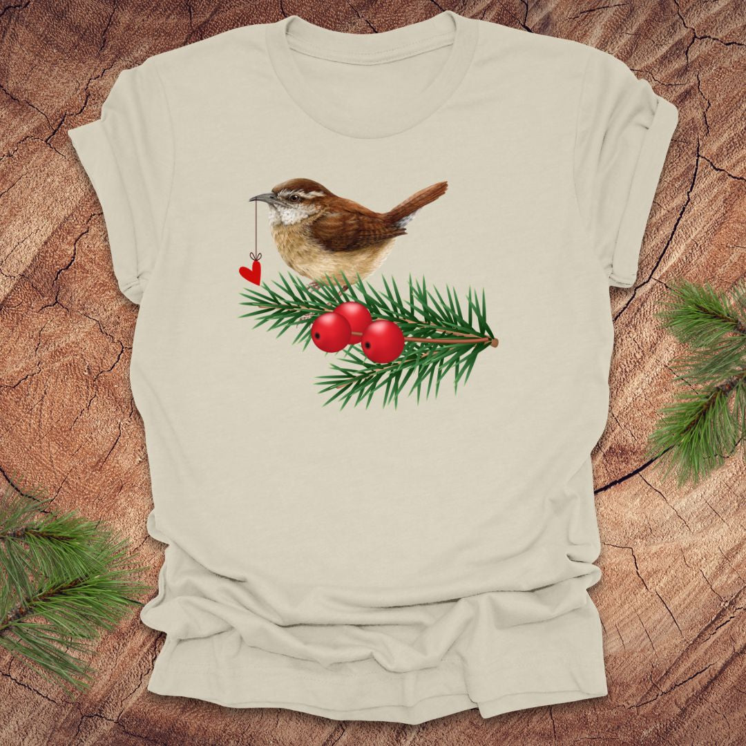 Beige t-shirt with a wren bird holding a heart on a string and holly design on a wooden surface