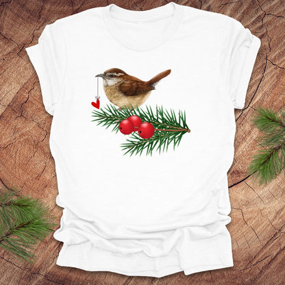 White t-shirt with a wren bird holding a heart on a string and holly design on a wooden surface