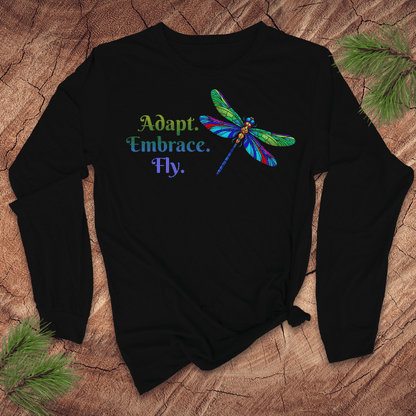 Black long-sleeve tshirt with colorful dragonfly design and text on a wood surface.