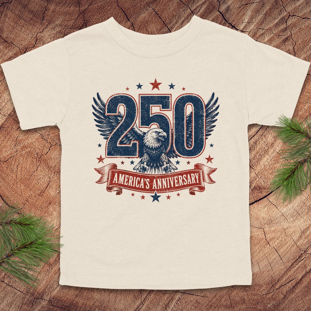 Beige t-shirt with '250 America's Anniversary' design on a wooden surface
