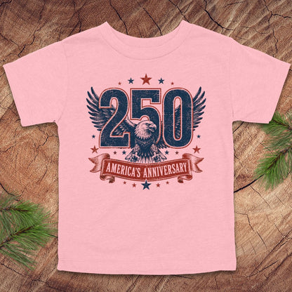 Pink t-shirt with '250 America's Anniversary' design on a wooden surface