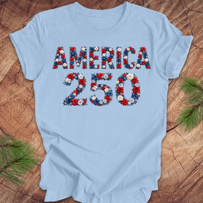 Light blue t-shirt with 'AMERICA 250' design featuring flowers on a wooden surface.