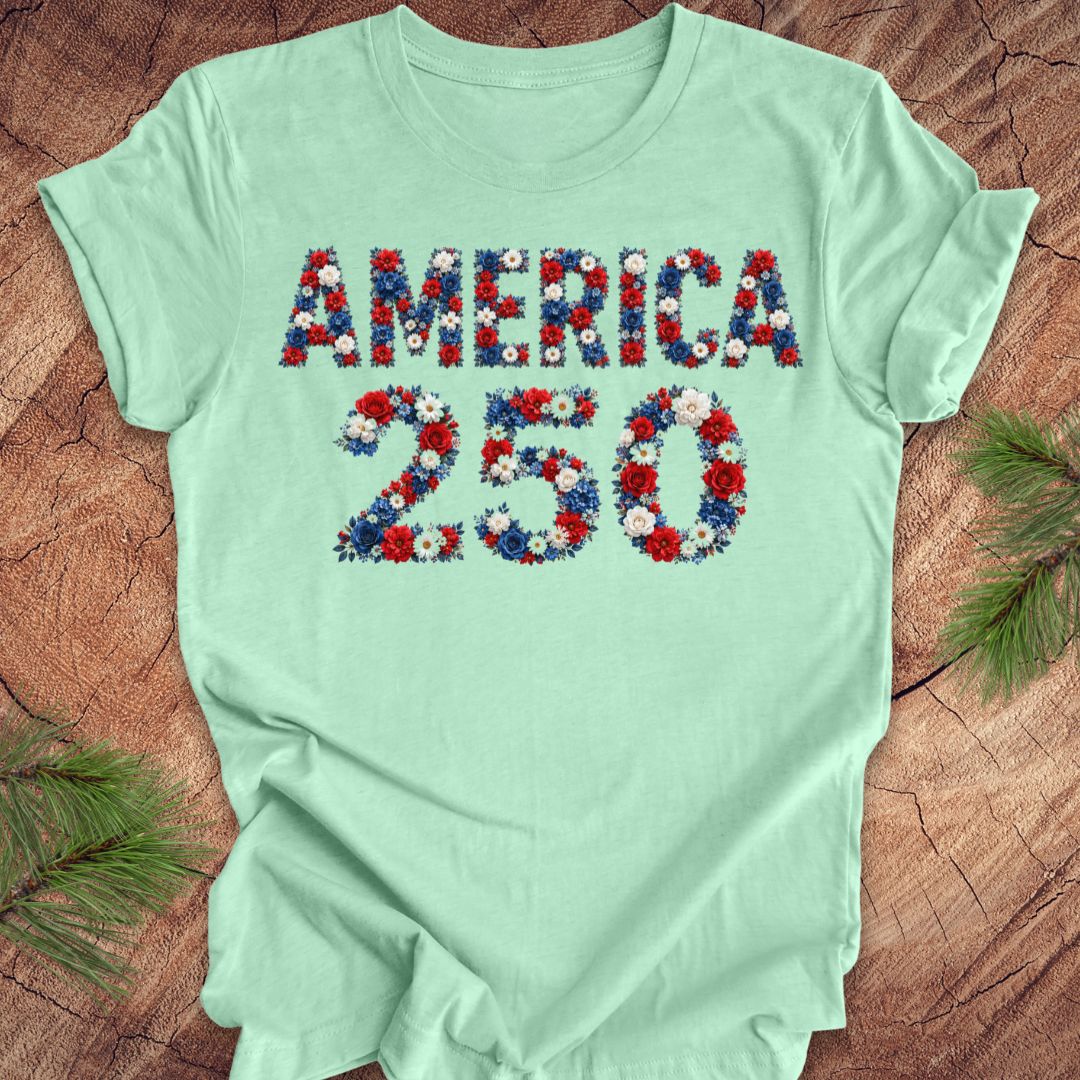 Mint green t-shirt with 'AMERICA 250' in floral letters on a wooden surface.