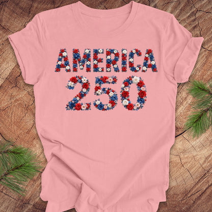 Pink t-shirt with 'AMERICA 250' design featuring flowers on a wooden surface.