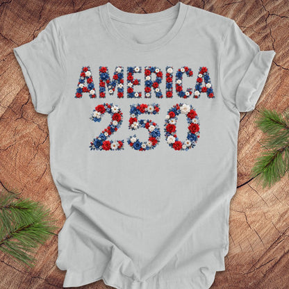 Gray t-shirt with 'AMERICA 250' design made of flowers on a wooden surface.