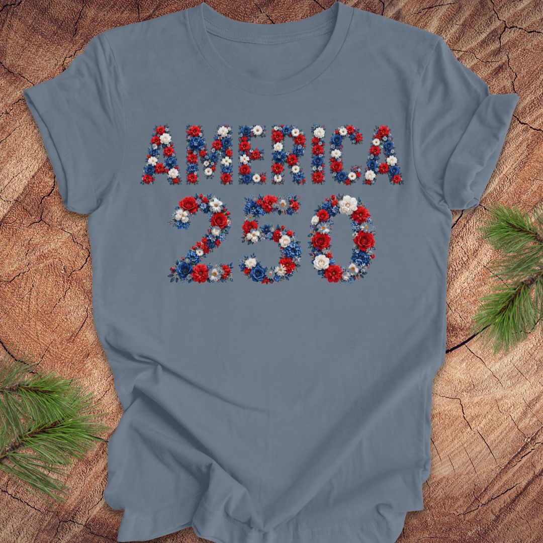 Blue t-shirt with 'AMERICA 250' design made of red, white, and blue flowers on a wooden surface.