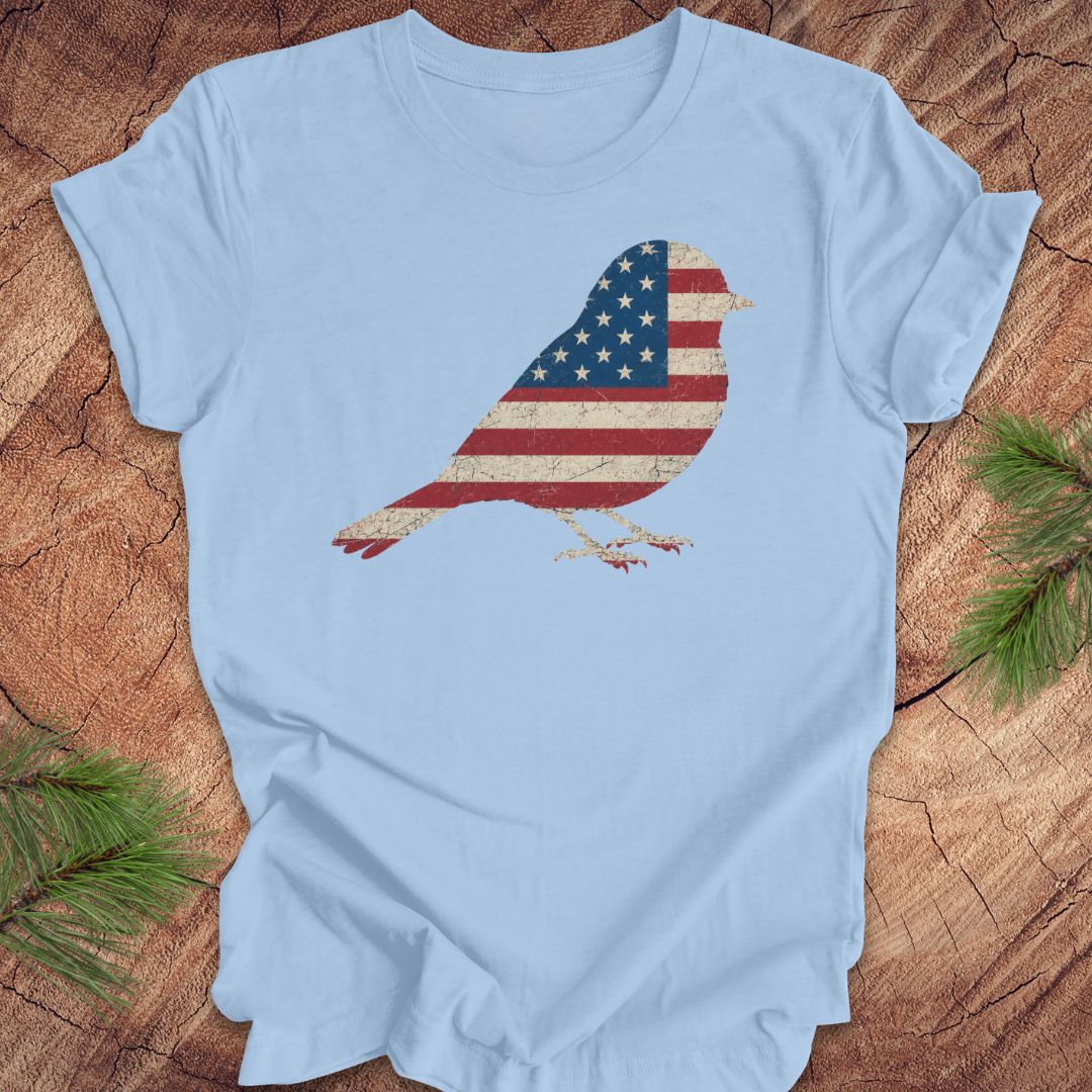Light blue t-shirt with a bird-shaped American flag design on a wooden surface.