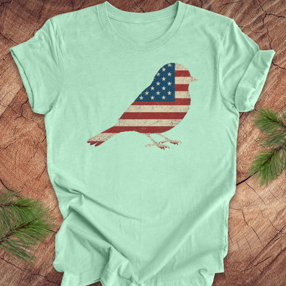 Mint green t-shirt with a bird design featuring an American flag on a wooden surface.