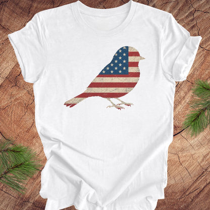White t-shirt with a bird design featuring the American flag on a wooden surface.