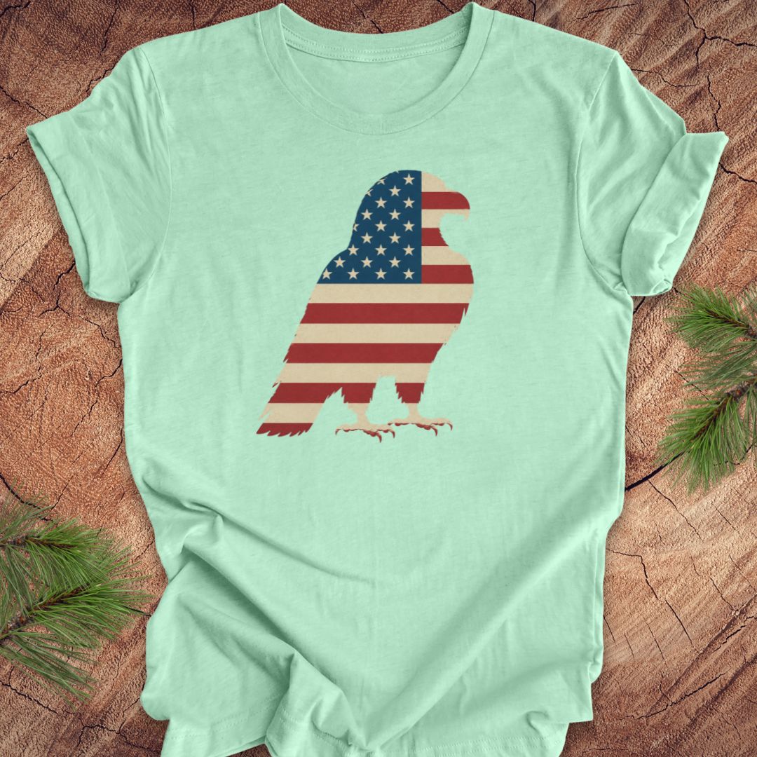 Light green t-shirt with an eagle silhouette in American flag colors on a wooden surface.