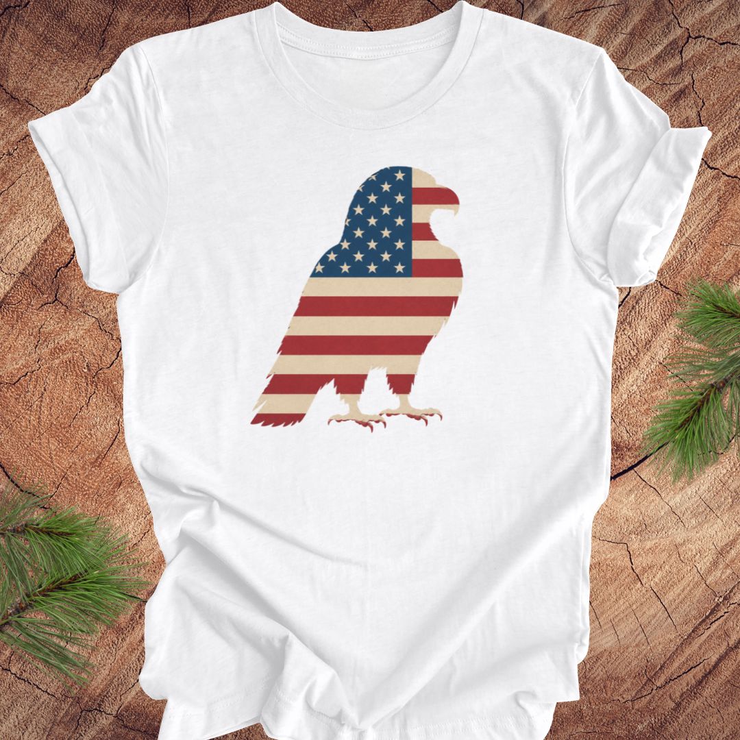 White t-shirt with an eagle design featuring the American flag on a wooden surface.