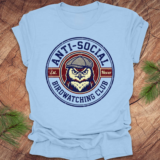 Light blue t-shirt with an owl graphic and text 'Anti-Social Birdwatching Club' on a wooden surface.