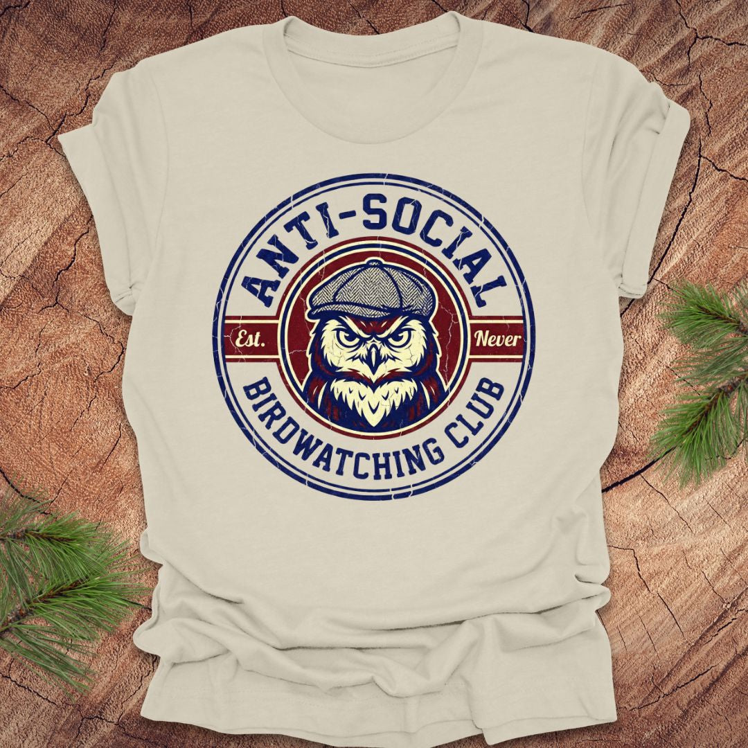 Beige t-shirt with 'Anti-Social Birdwatching Club' graphic on a wooden surface.